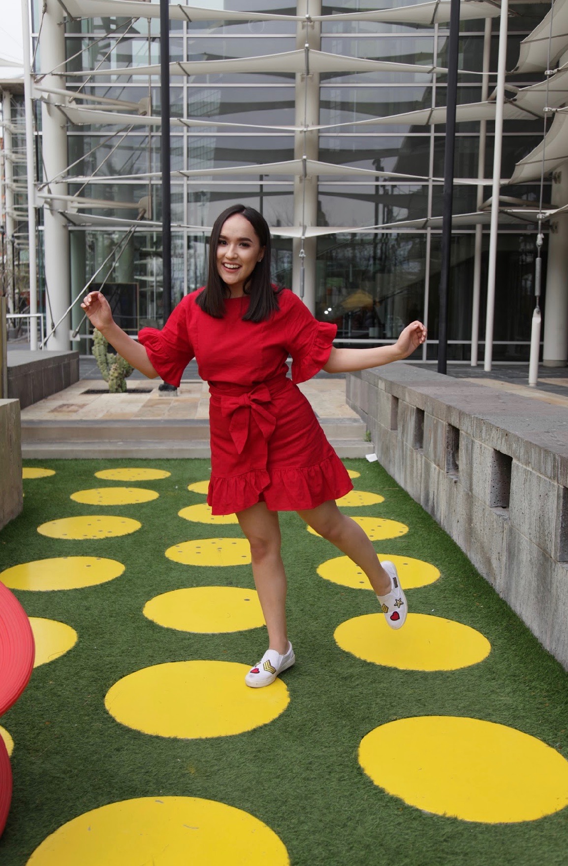 Melissa laughing and striking a playful pose outdoors in her red dress